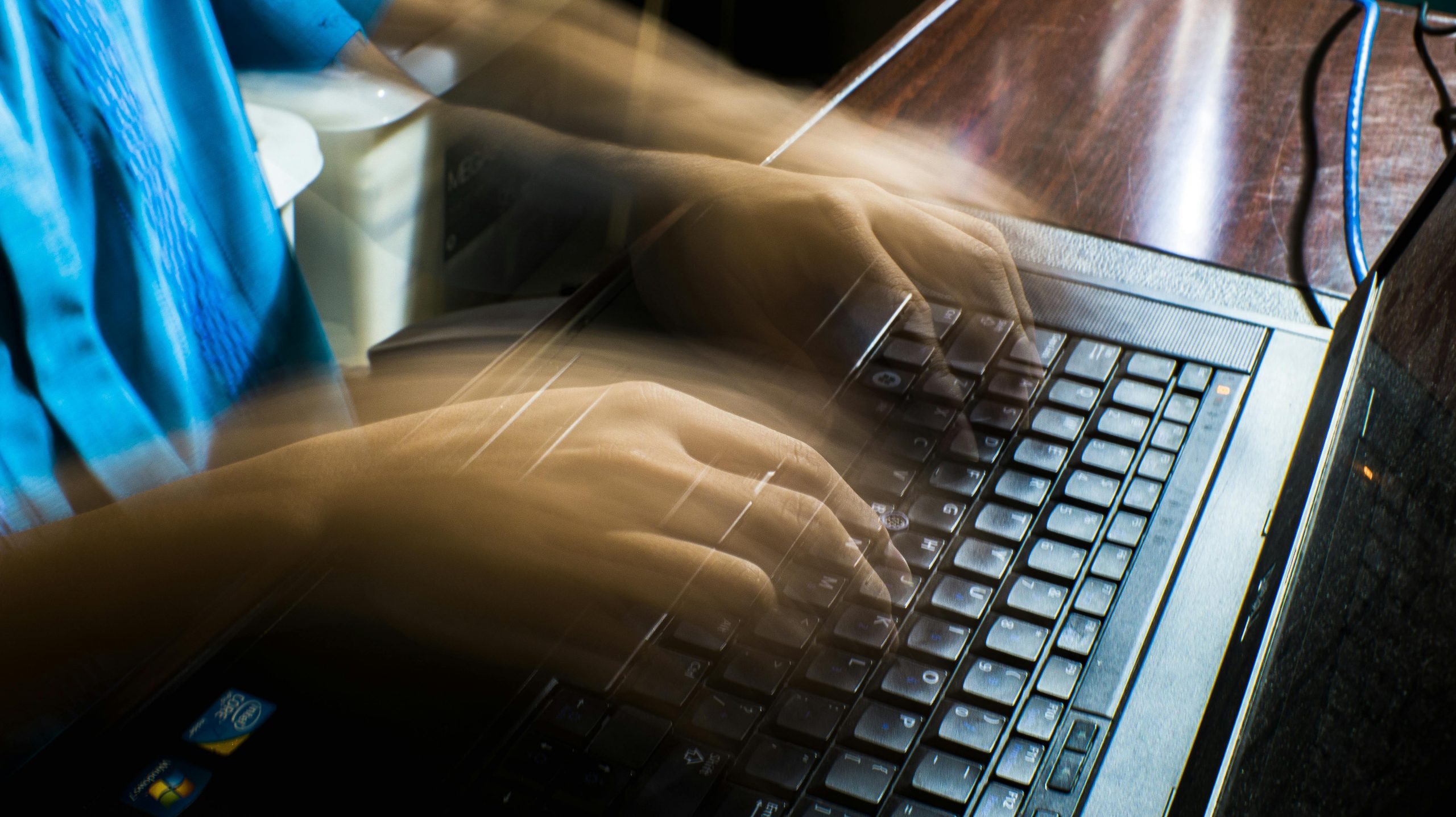 hands in motion blur rapidly typing on a laptop keyboard